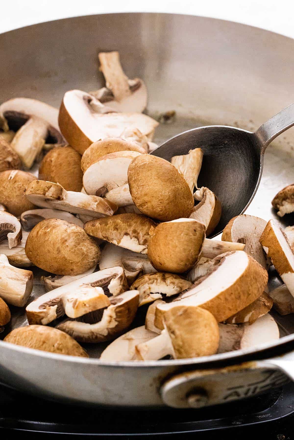 Sliced brown mushrooms cooking in a pan.