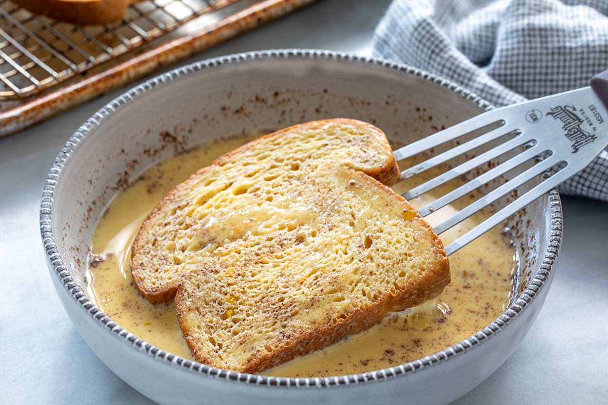 Dipping a slice of bread into bowl of egg and spice mixture.