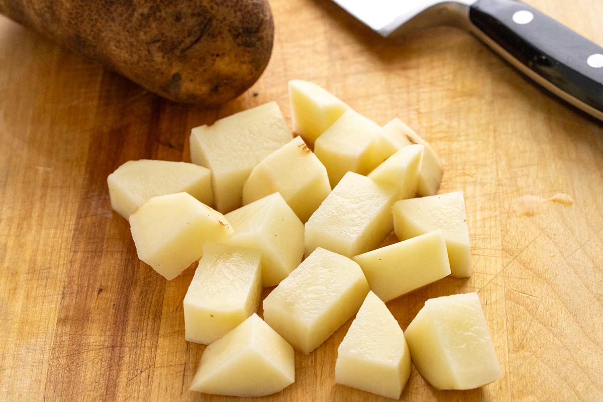 Peeled potatoes diced into three-quarter inch chunks on a wooden cutting board.