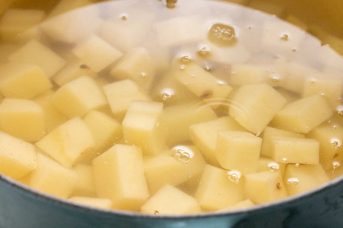 Diced peeled potatoes submerged in water in a cooking pot.