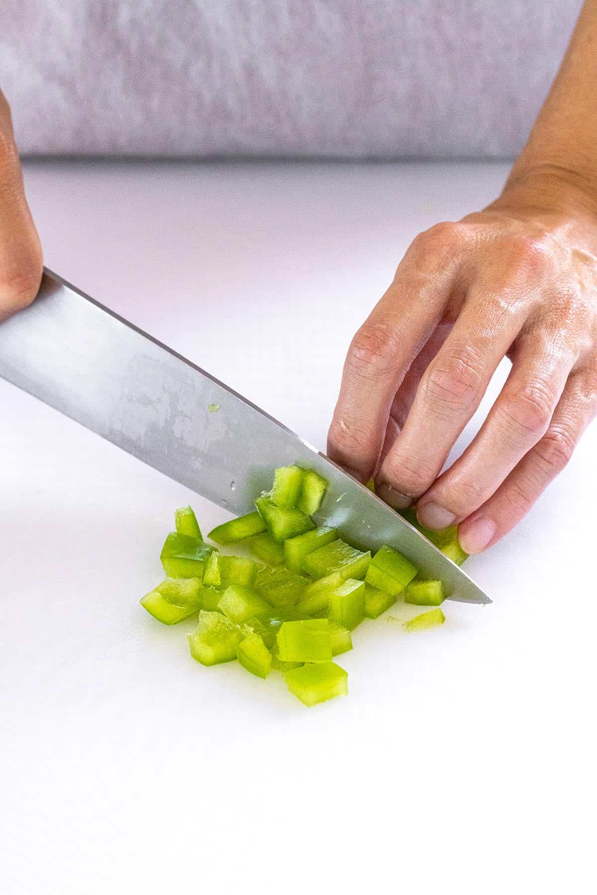 Person dicing a green bell pepper with a chefs knife.