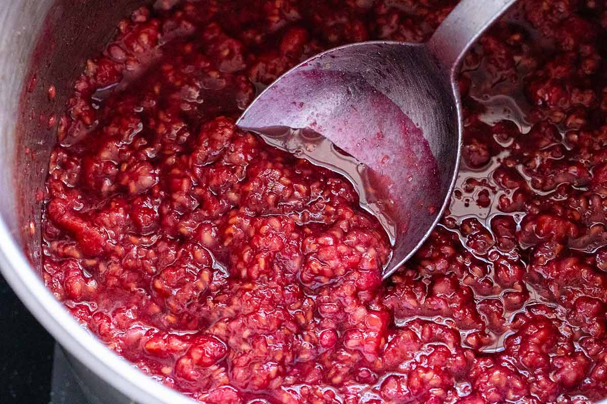 Raspberries, sugar, and lemon juice in a small saucepan being mixed with a metal spoon.