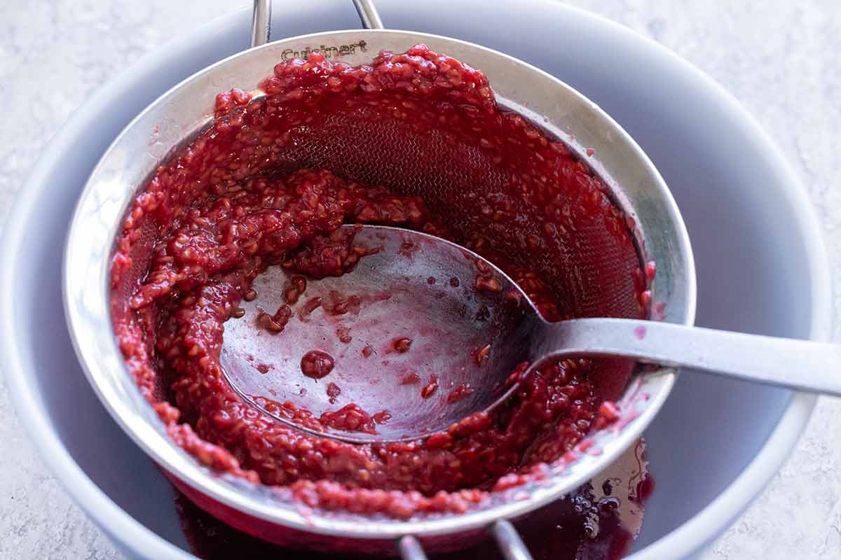 Raspberry sauce being pushed through a fine mesh stainer.