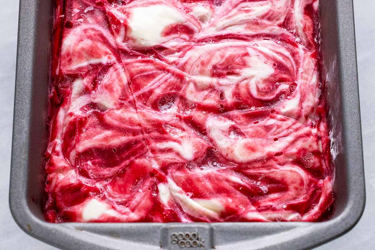 Frozen raspberry swirl ice cream in a metal pan.