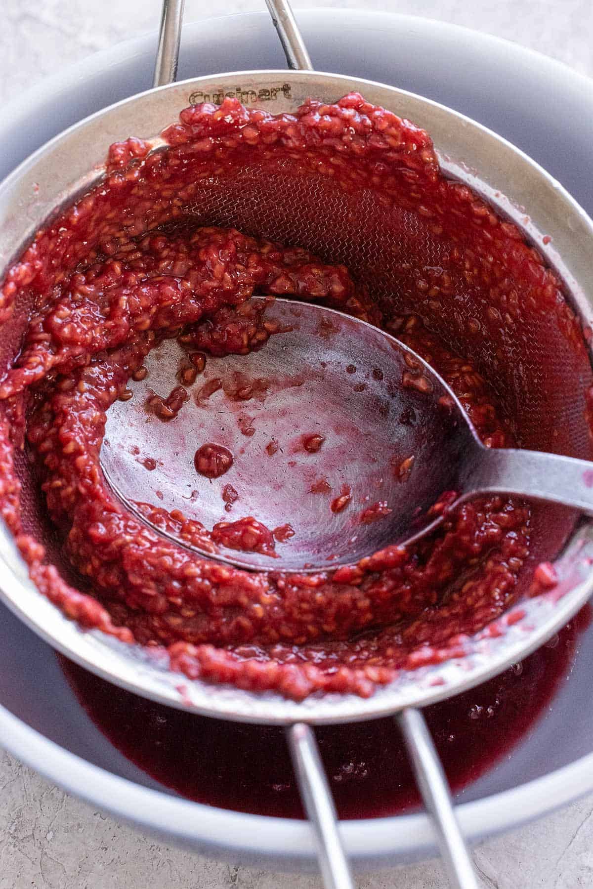 Raspberry sauce being pushed through a fine mesh stainer.