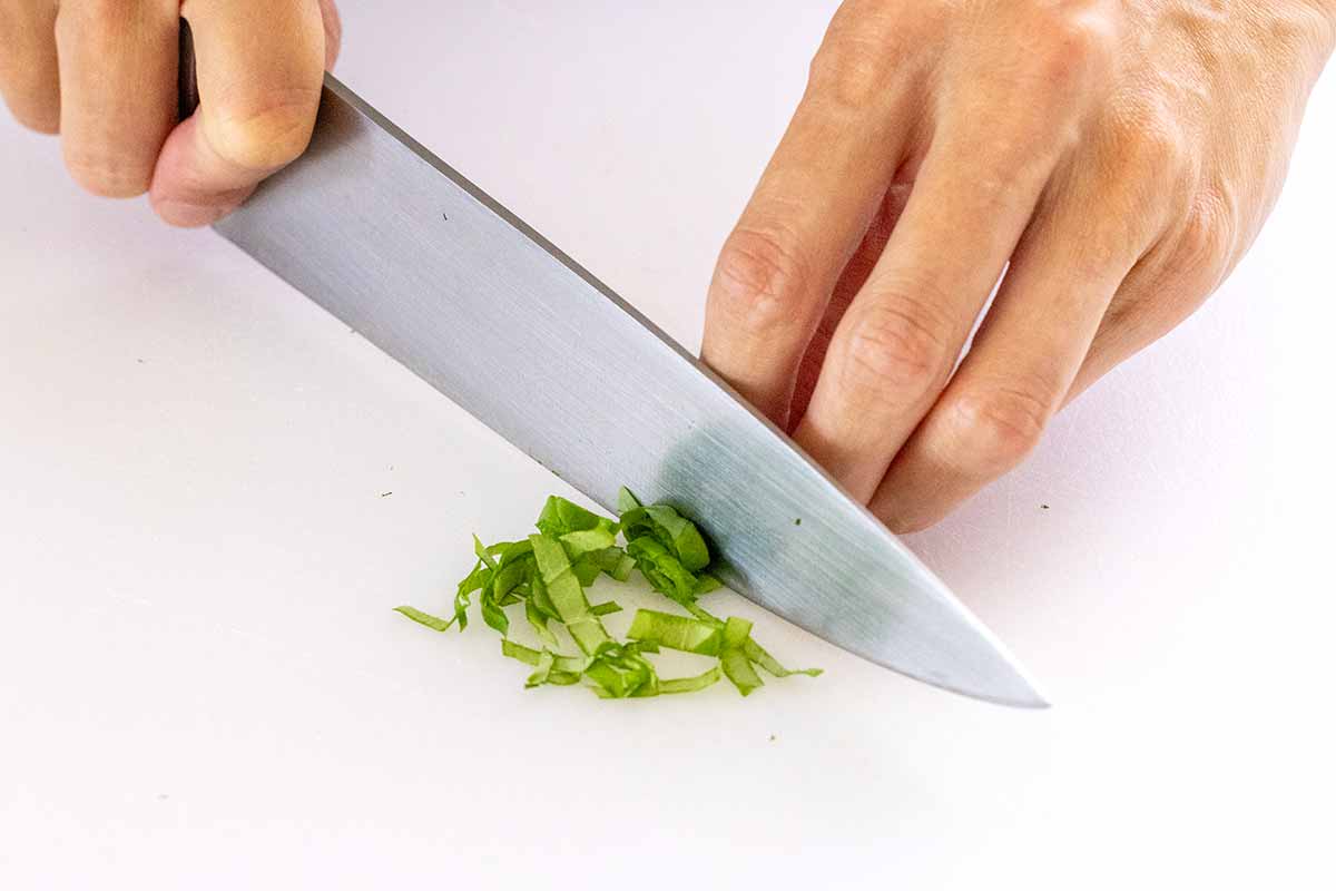 Chefs knife slicing through fresh basil leaves.