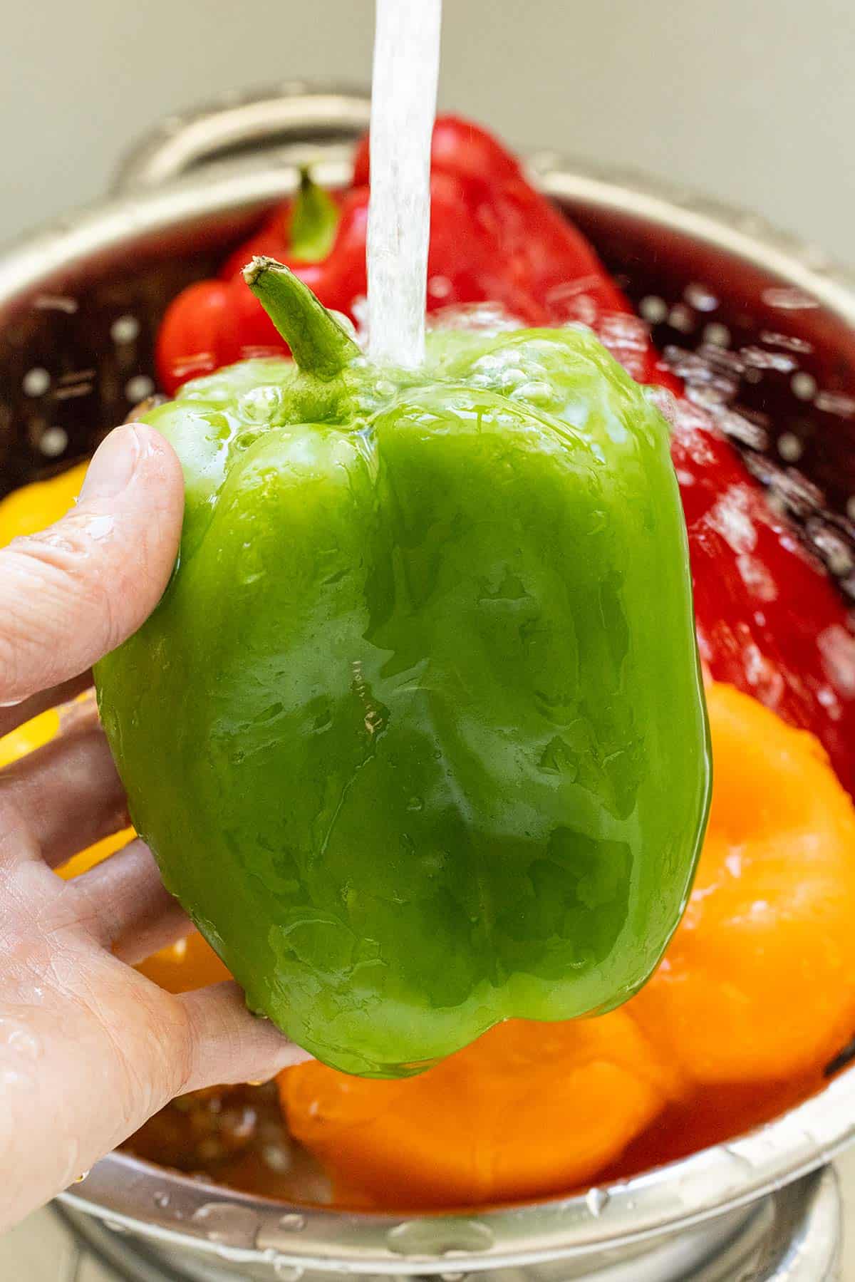 Person rinsing a green bell pepper under running water.