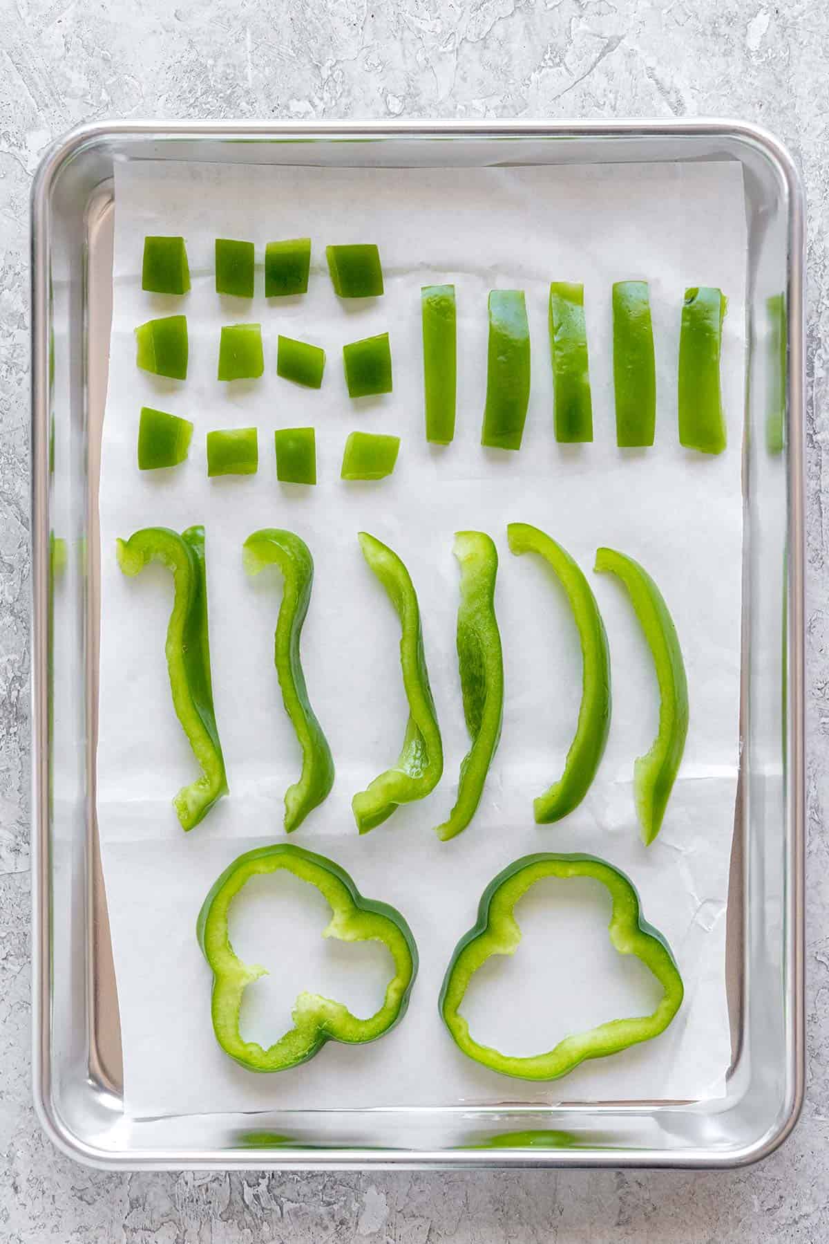 Green bell pepper cut into several shapes and places on a parchment paper lined sheet pan.