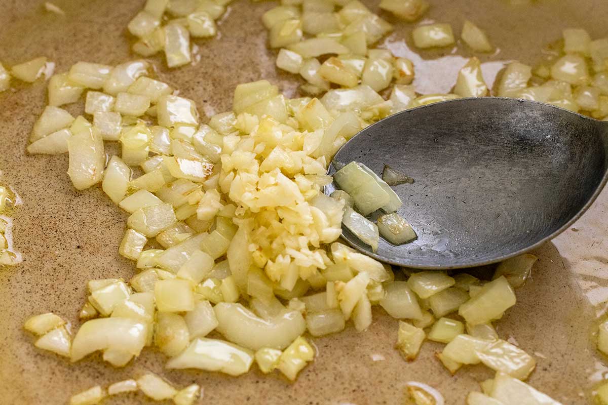 Diced onions and minced garlic sautéing in olive oil in a pot.