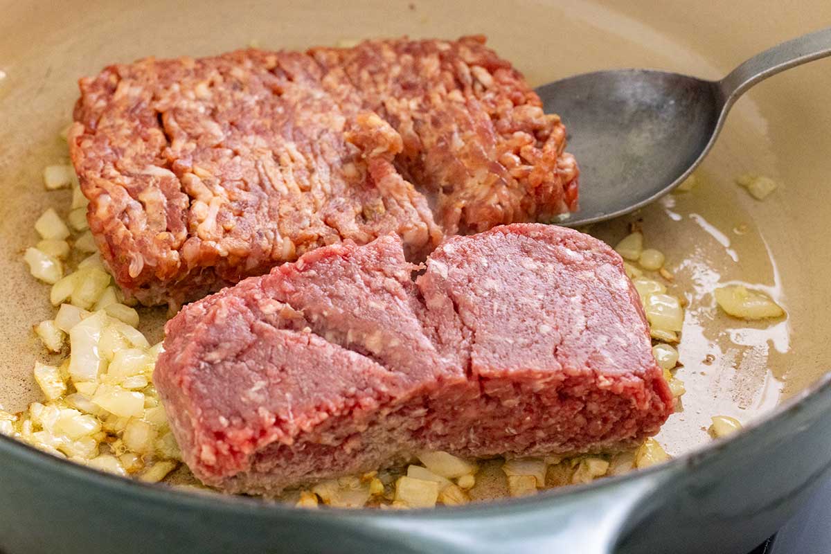 Raw ground beef and Italian sausage added to sautéed onions and garlic in a pot.