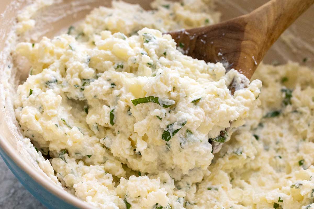 Ricotta cheese topping mixed with fresh herbs stirred in a bowl with a wooden spoon.