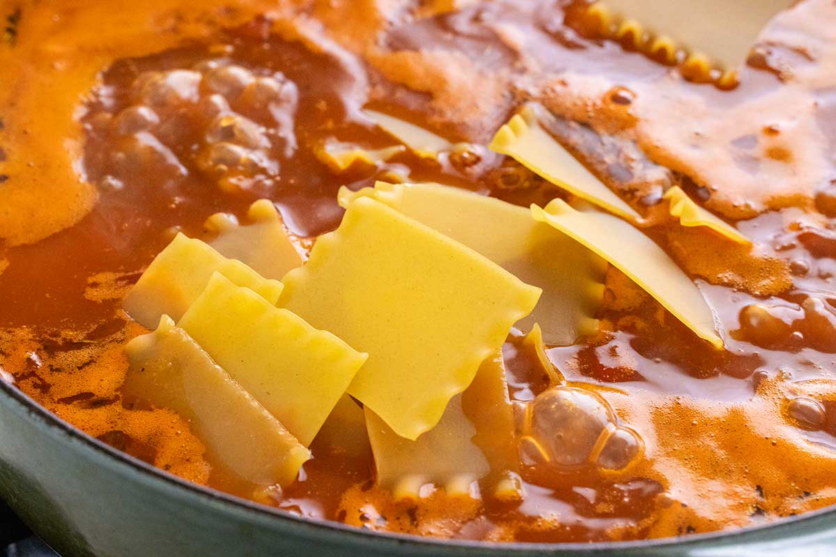 Broken lasagna noodle pieces added to a pot of bubbling tomato soup broth.
