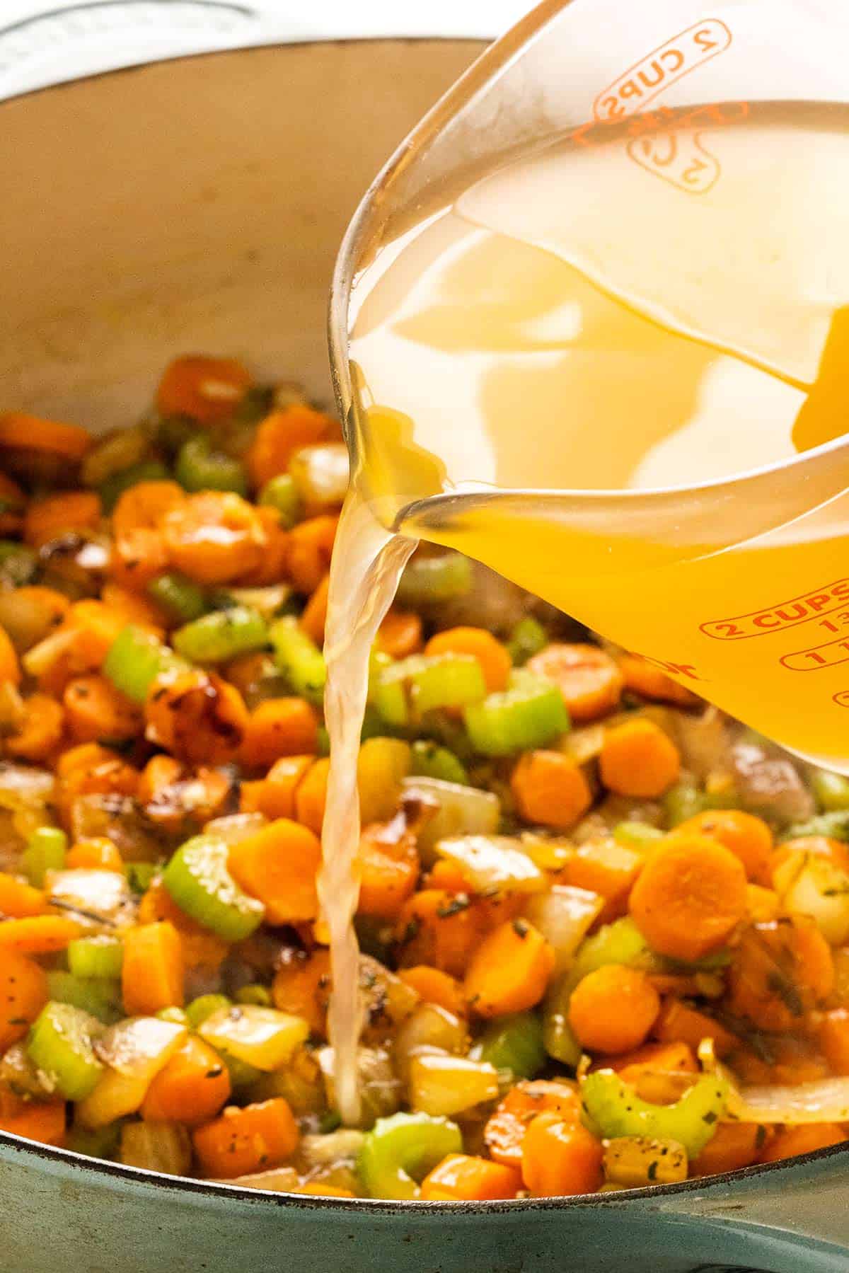 Pouring chicken stock into a pan of sauteed vegetables.