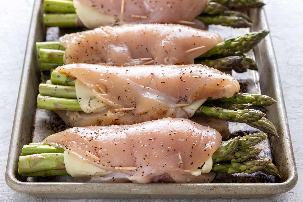 Four stuffed chicken breasts on a sheet pan ready to cook.