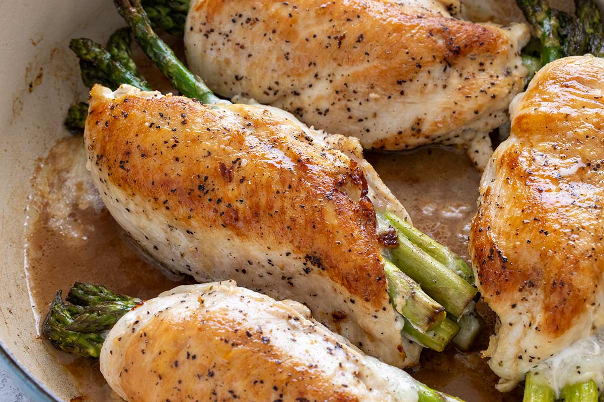 Asparagus stuffed chicken breasts with browned surfaces cooking inside a Dutch oven.