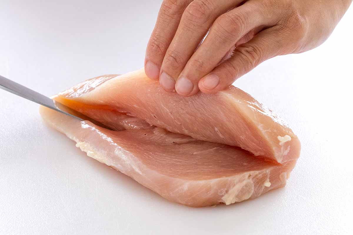 Chicken breast on a cutting board being sliced down the side.