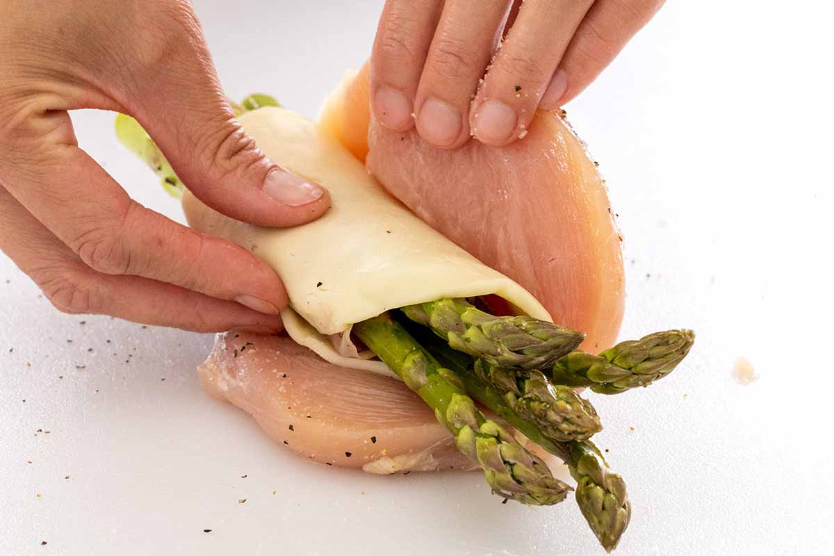Prosciutto and cheese wrapped asparagus bundle being placed inside a chicken breast.