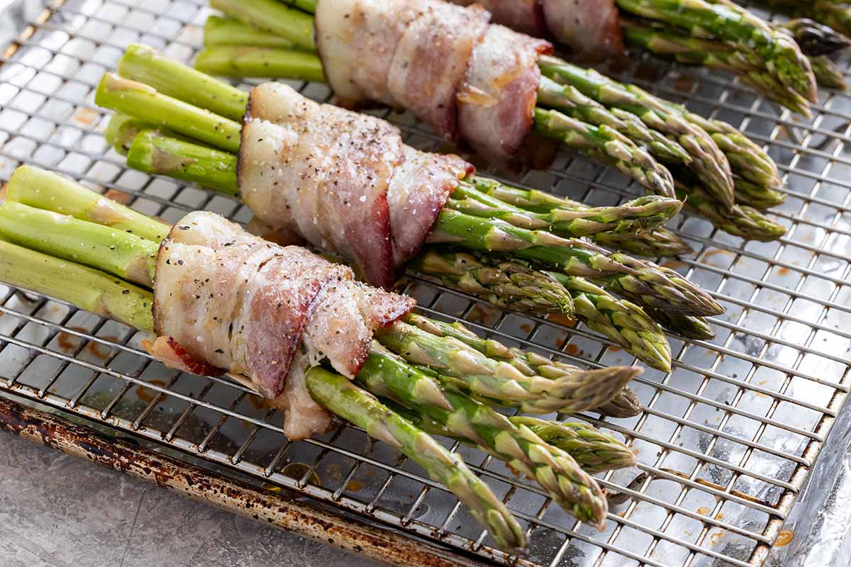 Several bacon wrapped asparagus on a wire rack ready to go in the oven.
