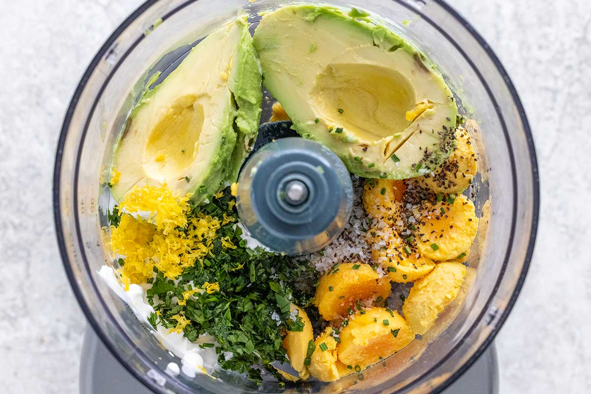 Egg yolks, avocado slices, and spices in a food processor.