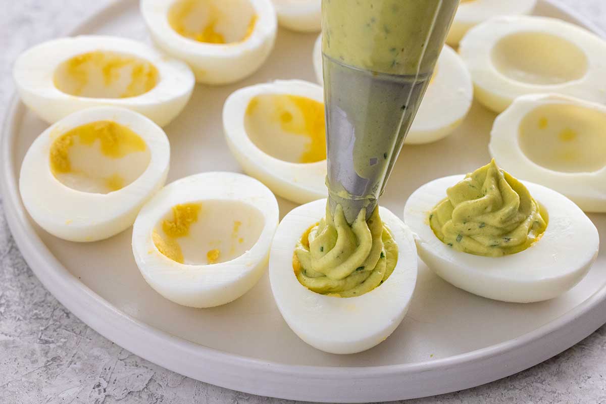 Piping greenish colored egg filling mixture into the cavity of a hardboiled egg white.