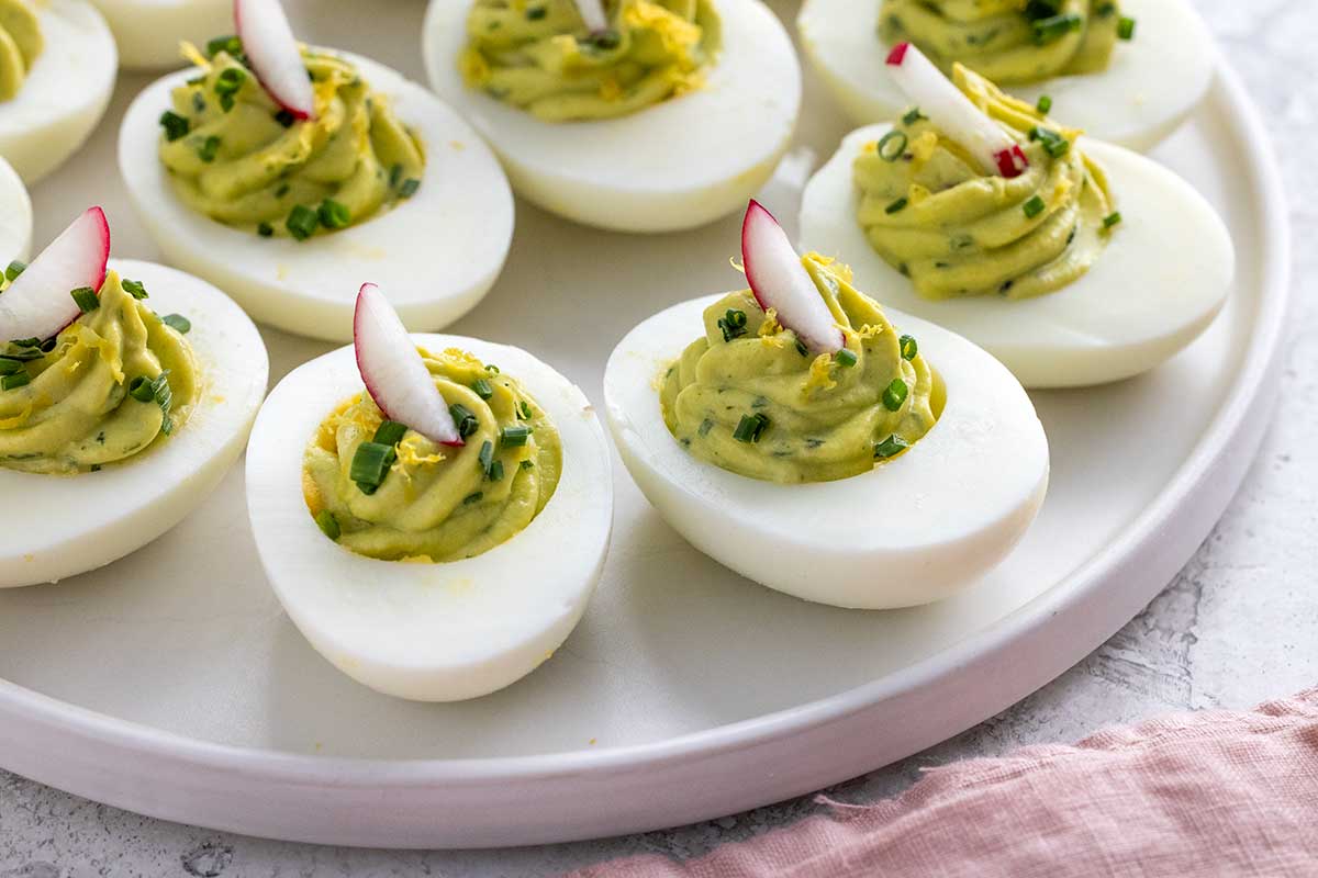 Avocado deviled eggs garnished with radish and chives, and served on a white platter.