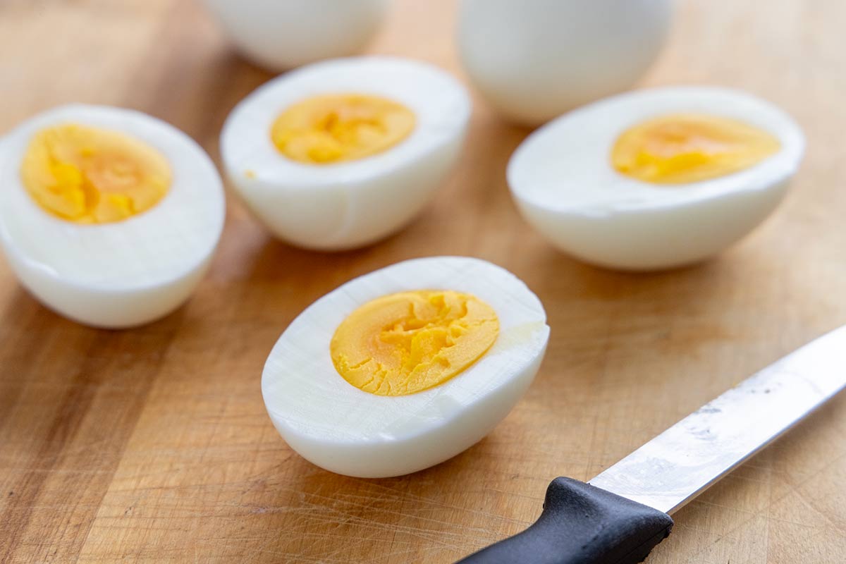 Several hard-boiled eggs on a cutting board that have been split in half.