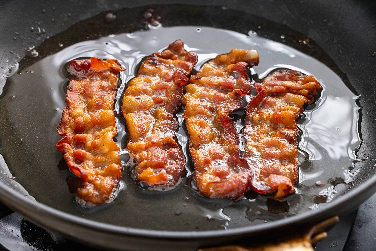 Four strips of bacon cooking in a pan on the stovetop.