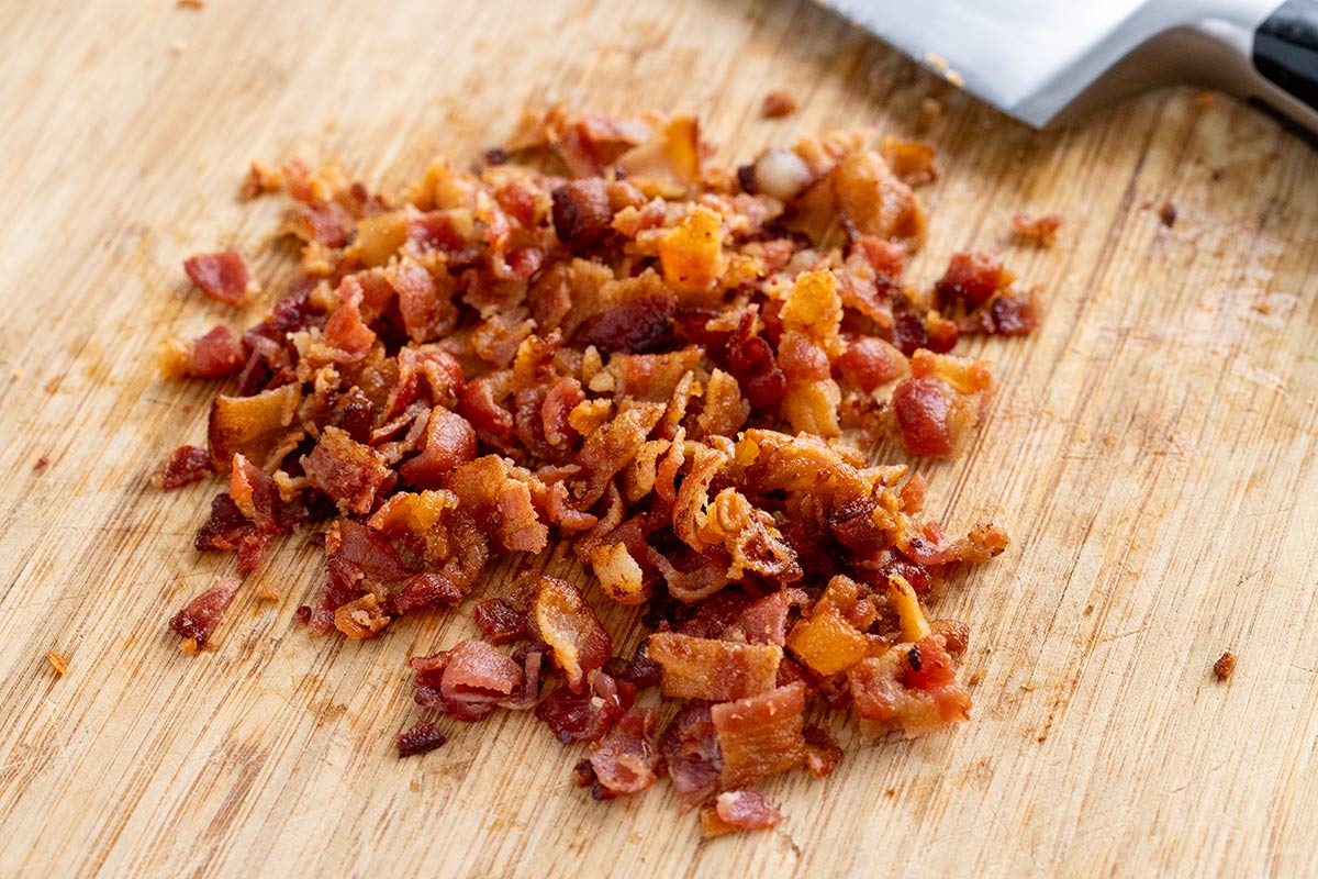 Crispy bacon on a wooden cutting board that have been chopped into smaller pieces.
