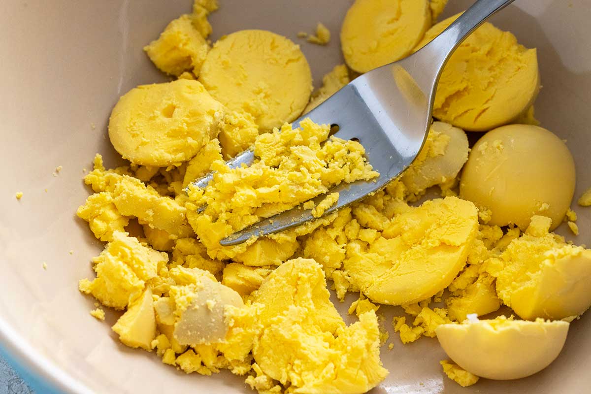 Bowl of egg yolks mashed into pieces using a fork.
