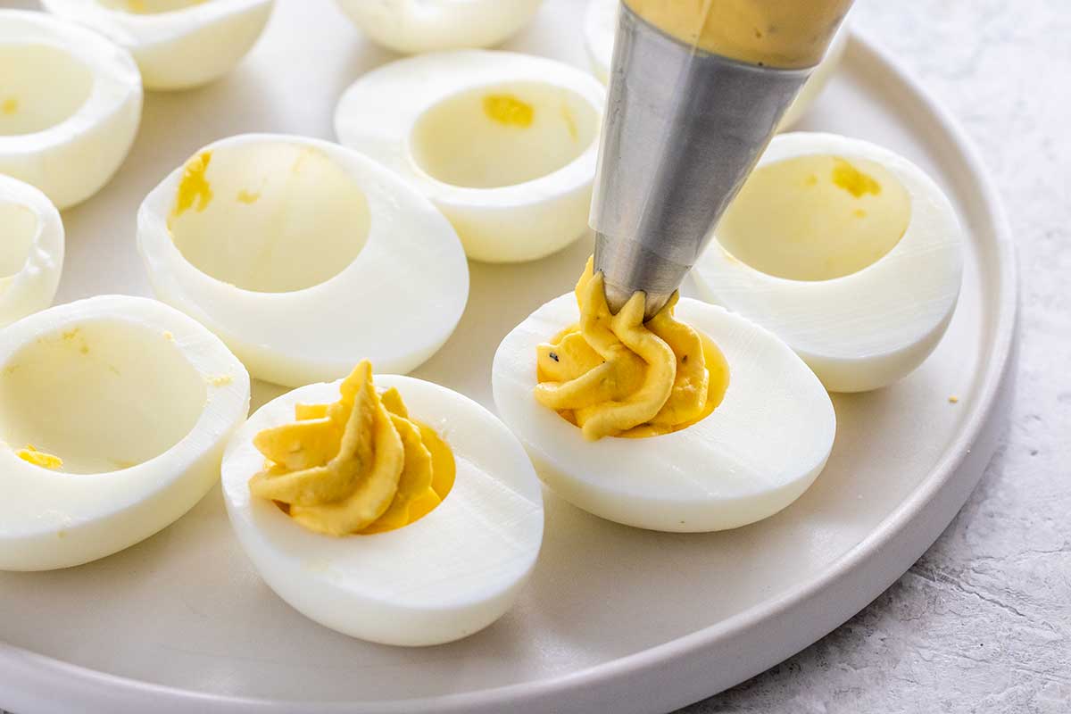 Piping yolk mixture into the cavity of a hard-boiled egg.