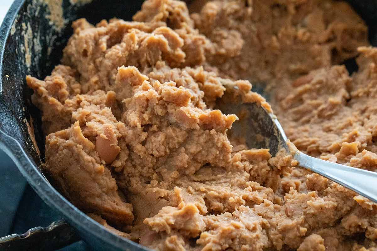 Spoon stirring refried beans being heated up in a cast iron skillet.