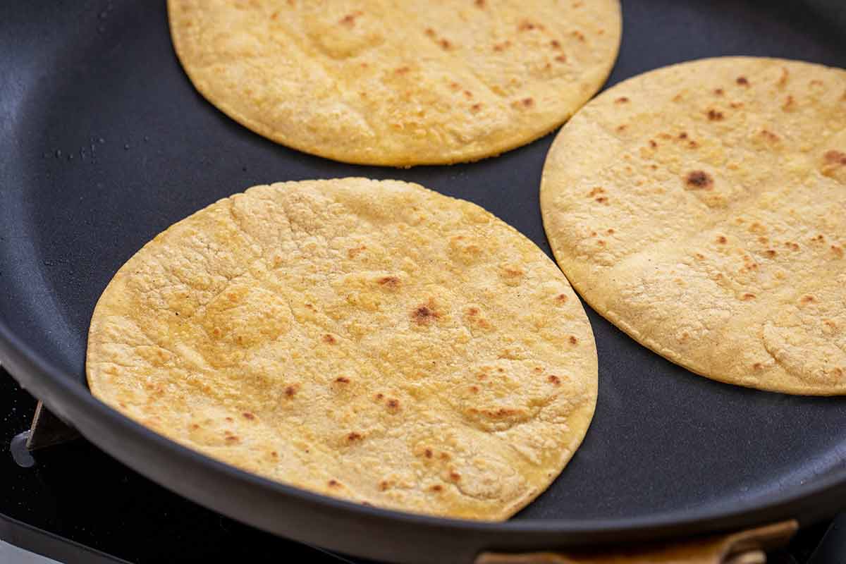 Three corn tortillas in a non stick frying pan.