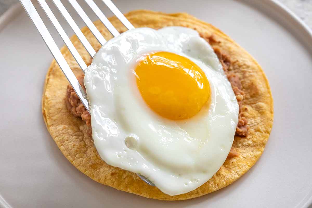 Placing a fried egg on top of the beans and tortilla.