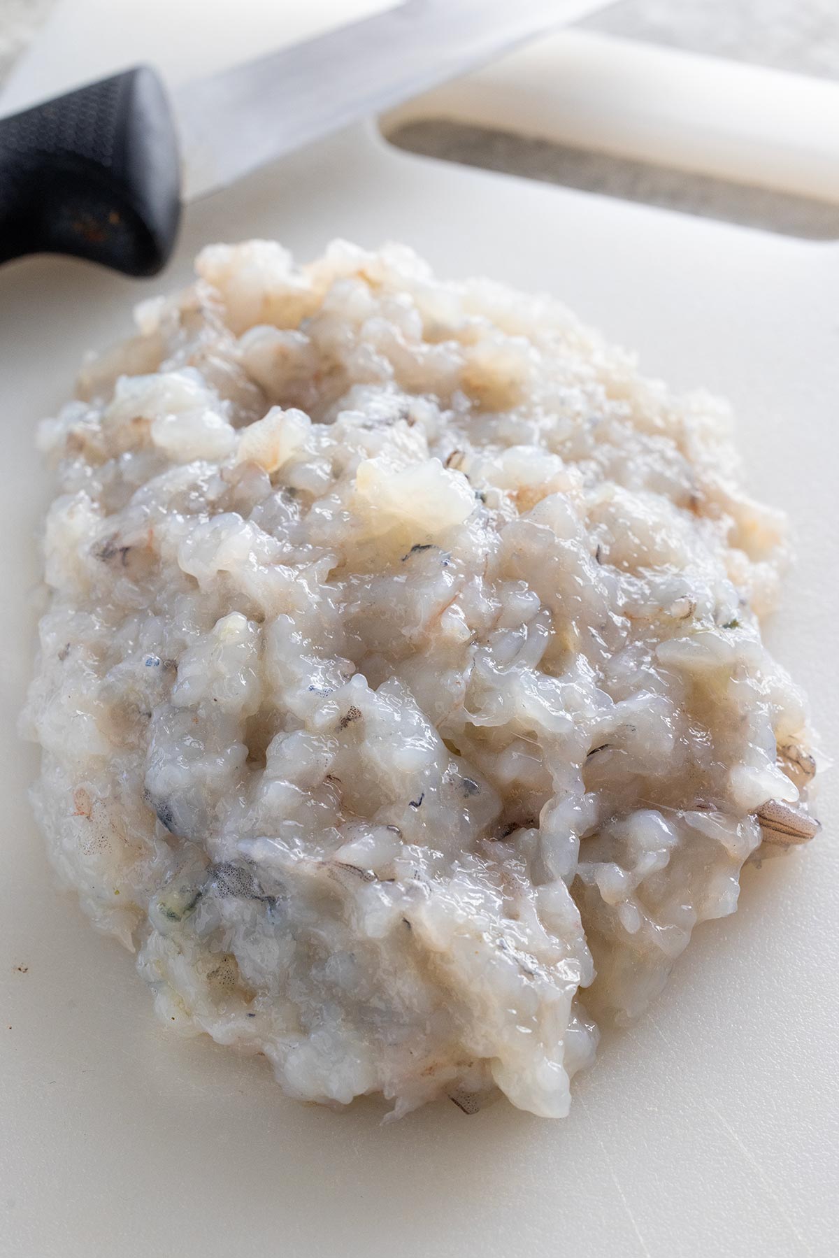 White cutting board with shrimp chopped and mashed into a paste.