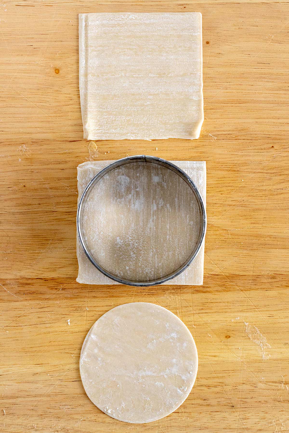Wonton wrappers on a cutting board being cut into a circle.