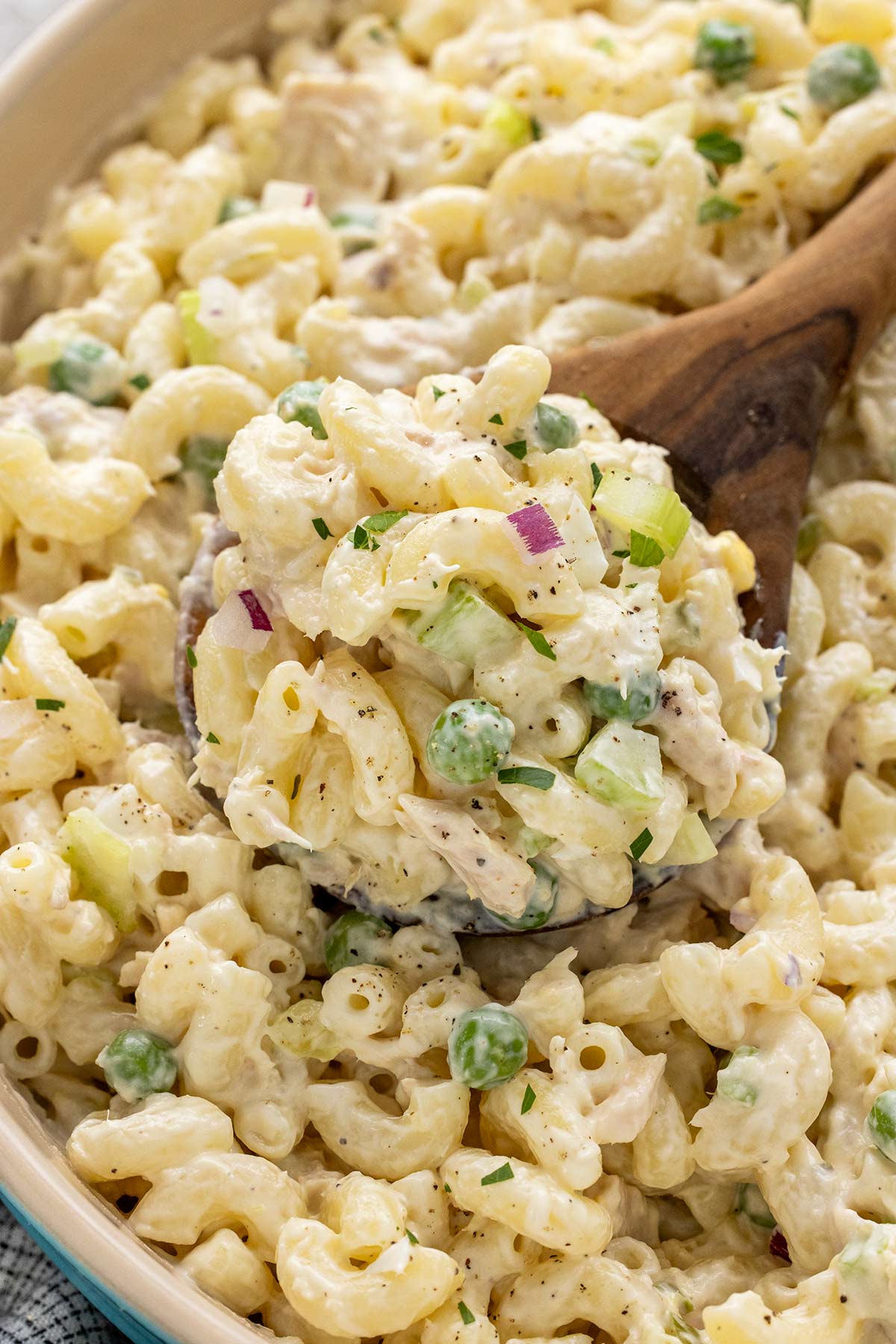 Wooden spoon mixing a bowl of tuna mac salad.