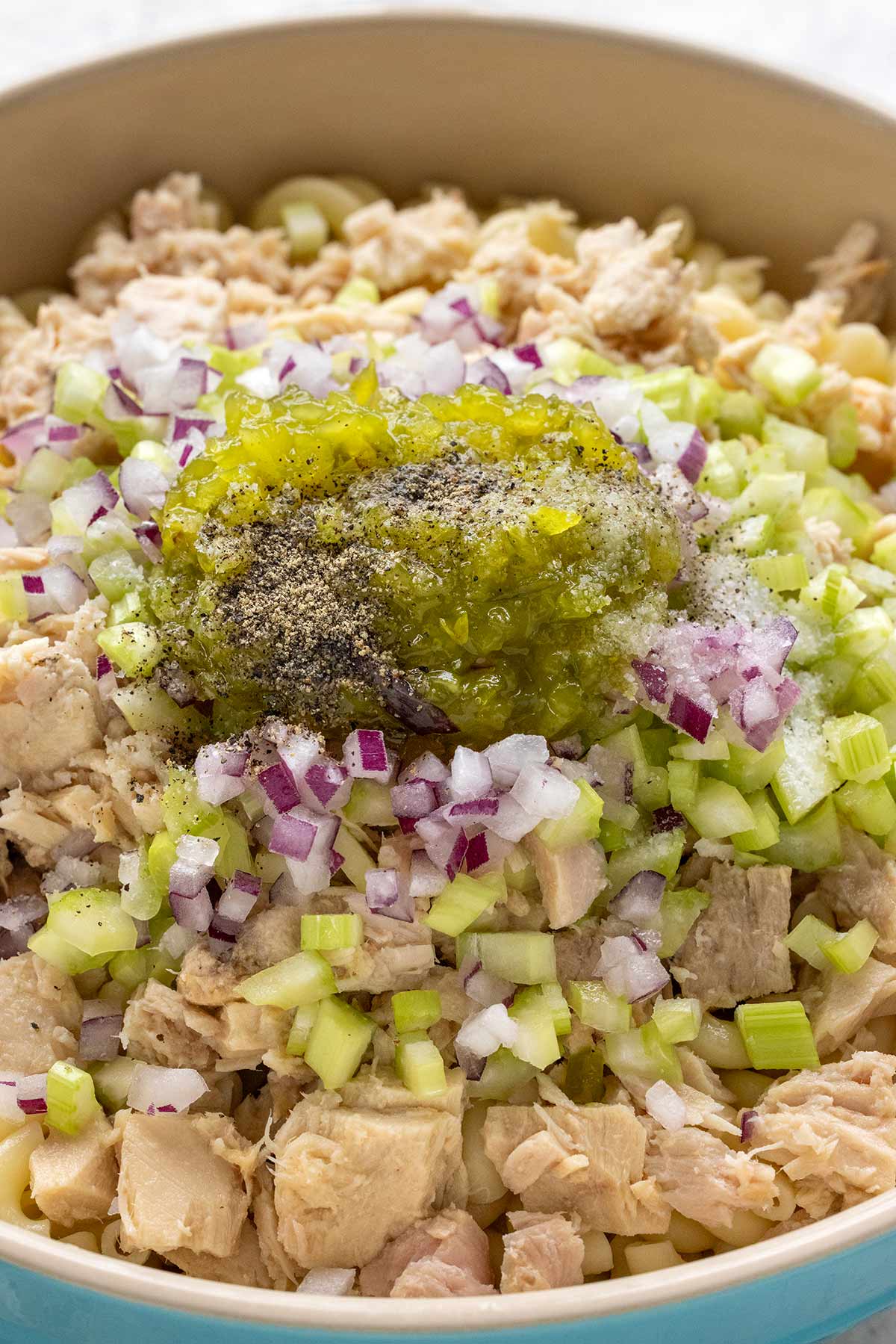 Relish, red onions, and chunks of albacore tuna in a mixing bowl.