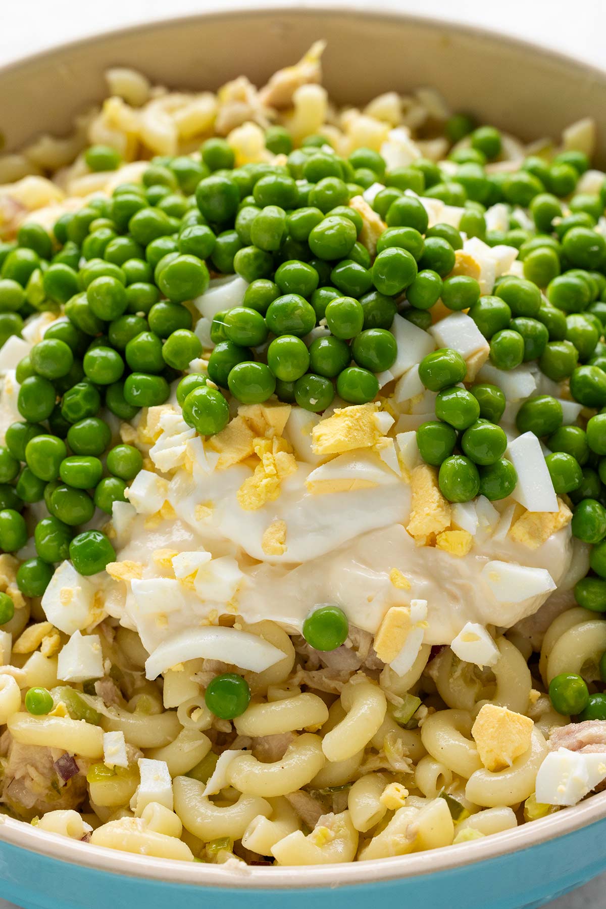 Pea and chopped hard boiled eggs added to a bowl of macaroni and tuna.