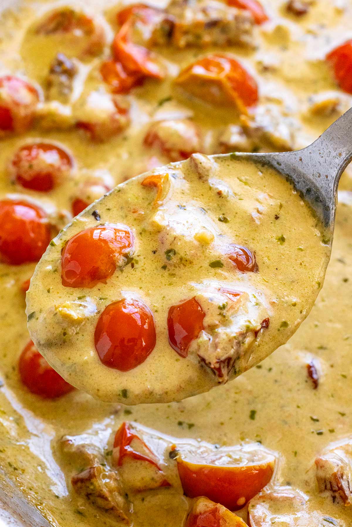 Creamy pesto sauce and cherry tomatoes being lifted out of a pan.