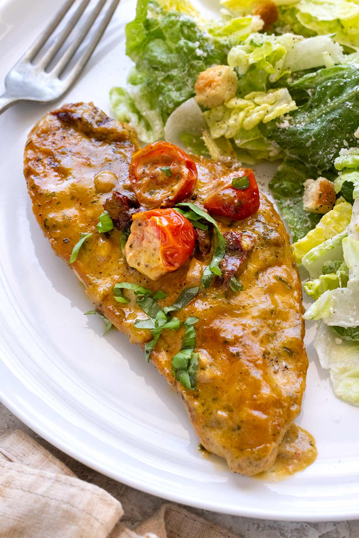 Serving of pesto chicken and salad on a white plate.