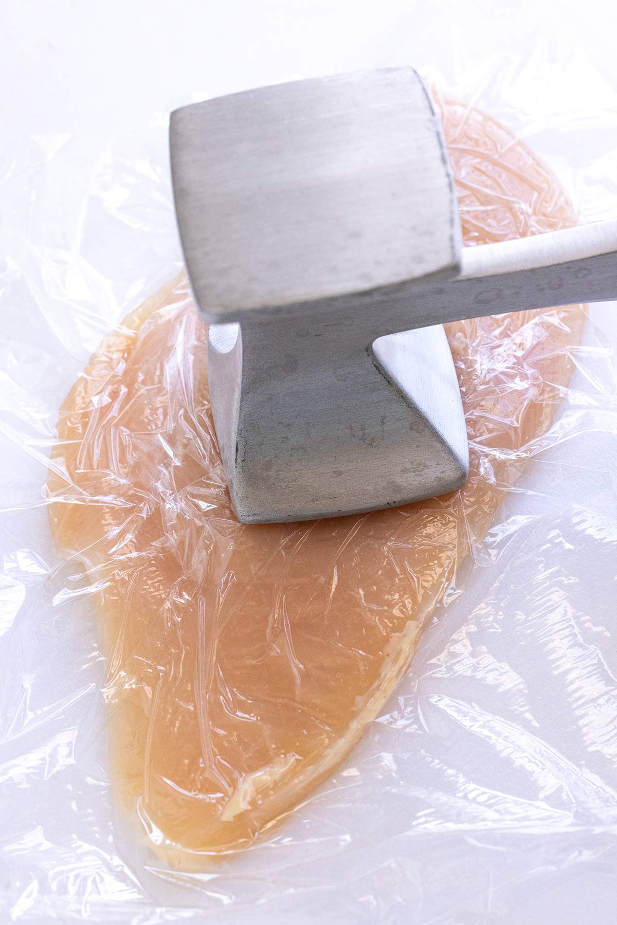 Meat tenderizer being used on a chicken breast.