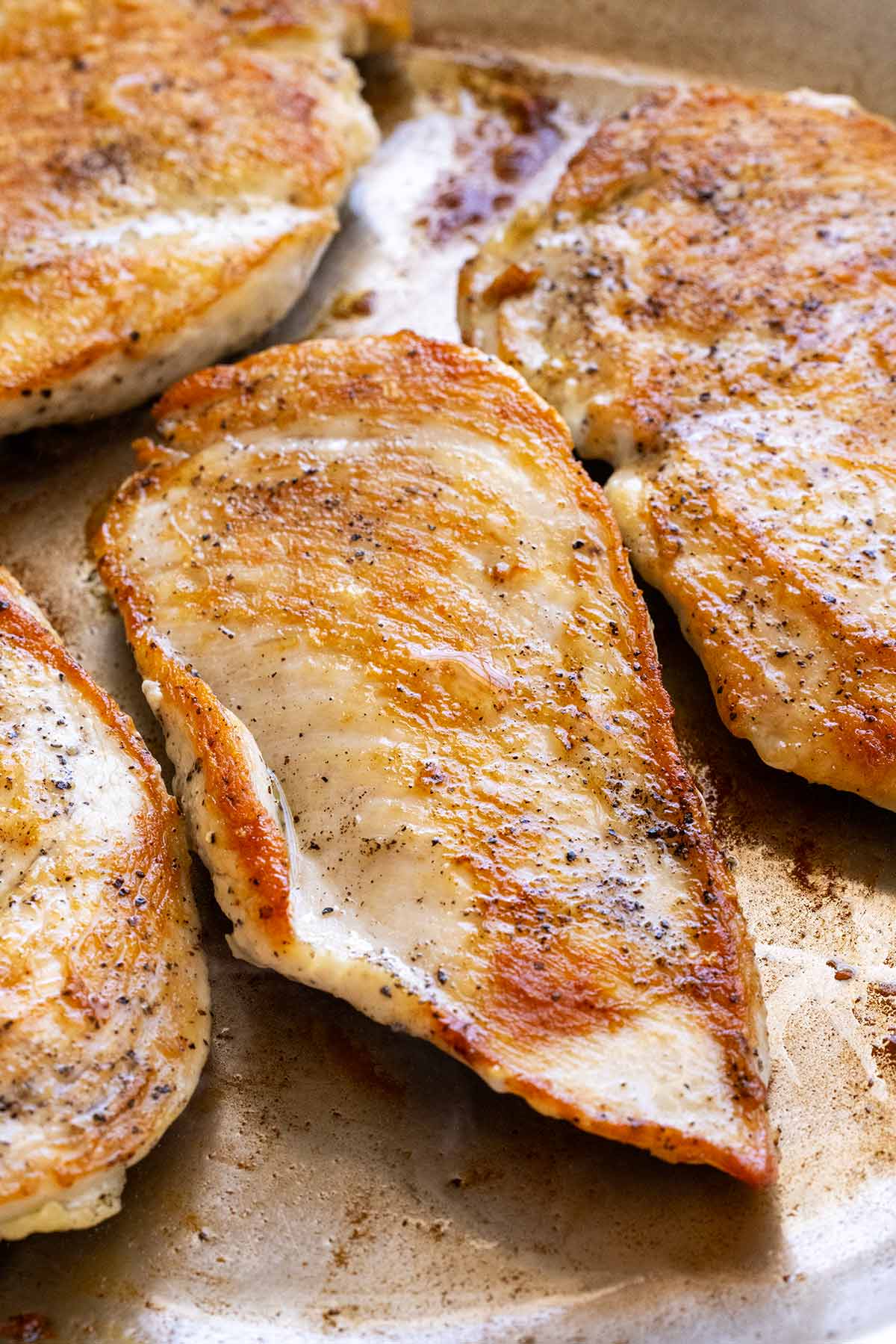 Several boneless, skinless chicken breasts searing in a pan.
