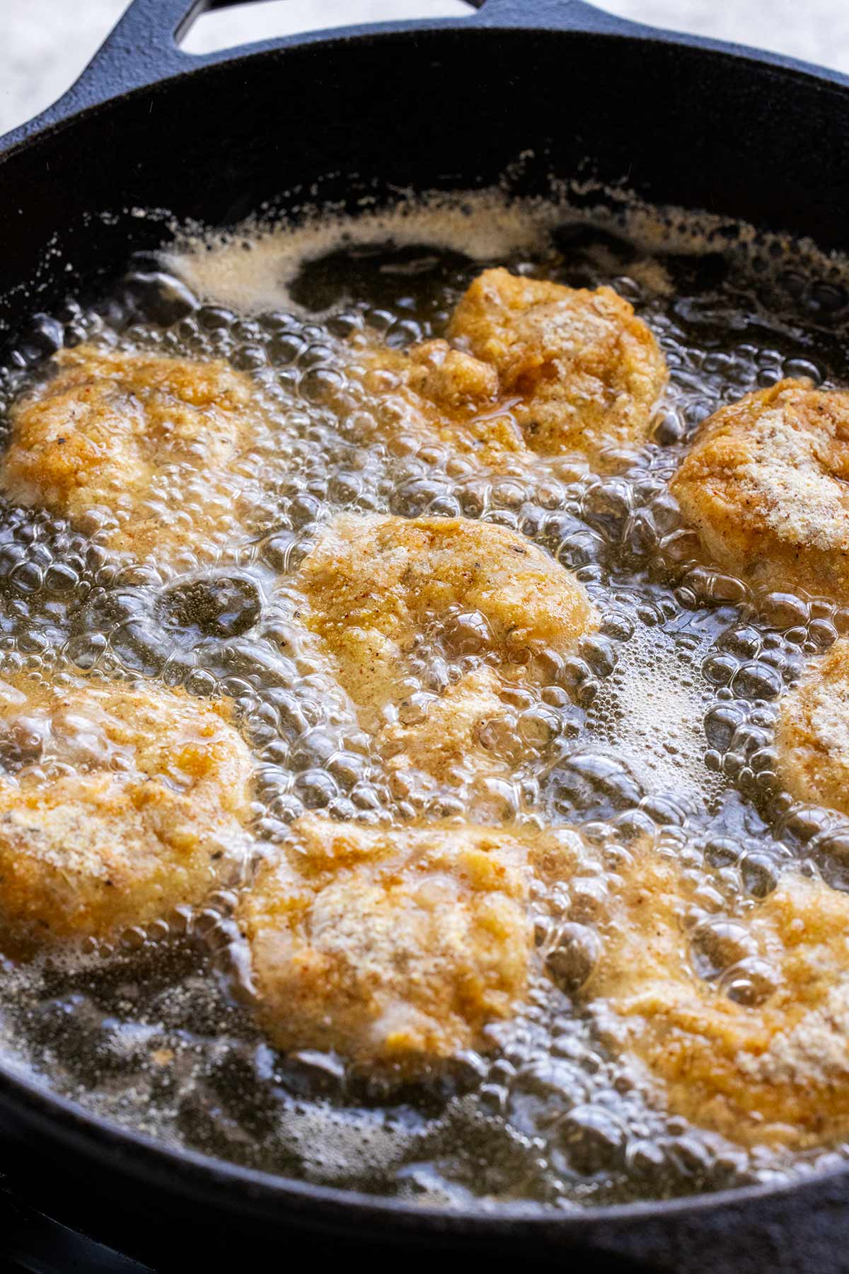 Several pieces of shrimp frying in a cast iron skillet with oil.