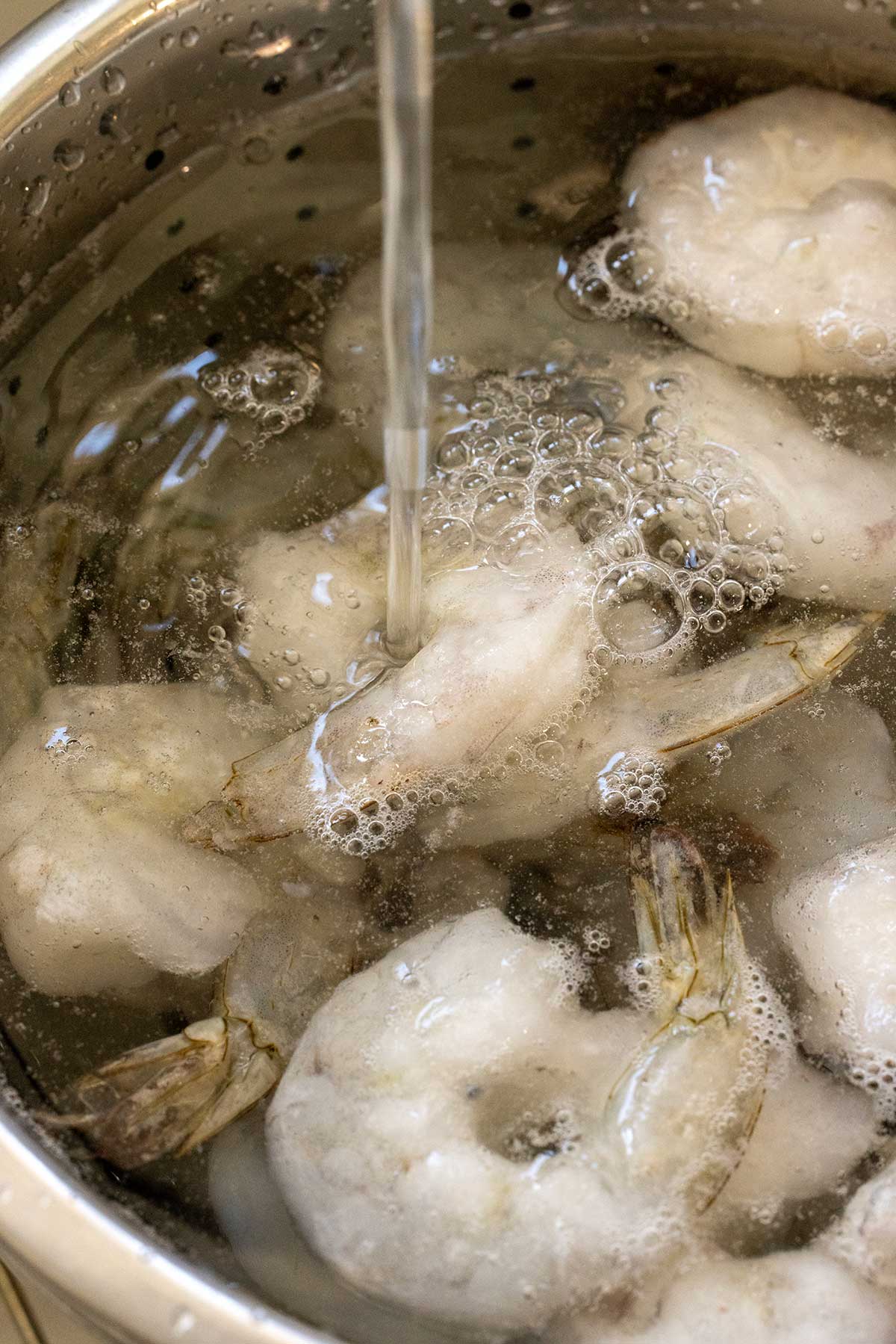 Frozen shrimp in a colander being rinsed with water.