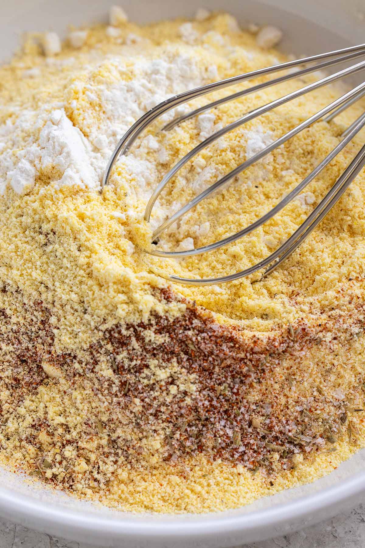 Whisk mixing a bowl of cornmeal, flour, and spices.
