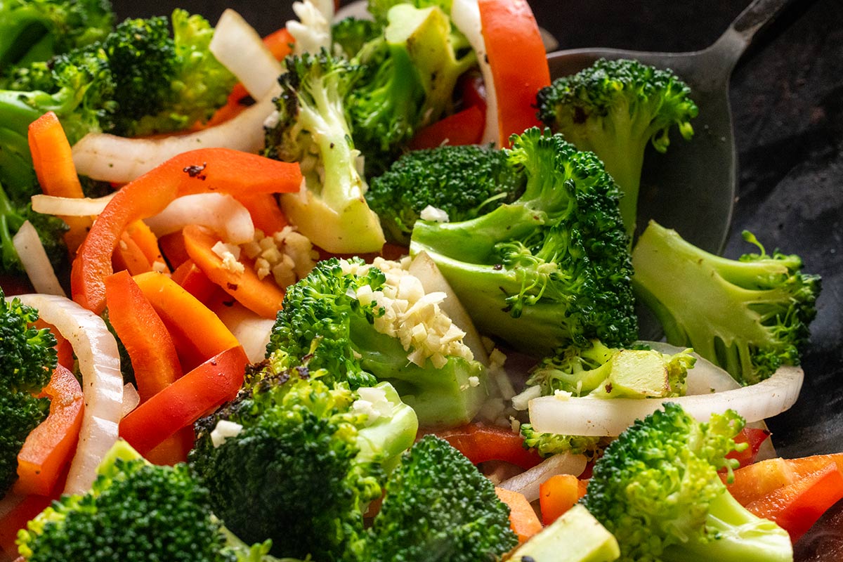 Broccoli, onions, and peppers being cooked and tossed in a wok.