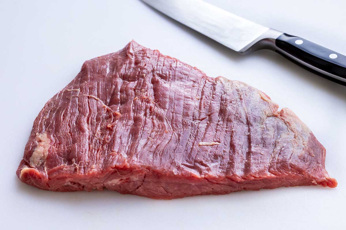 Piece of flank steak on a white cutting board.