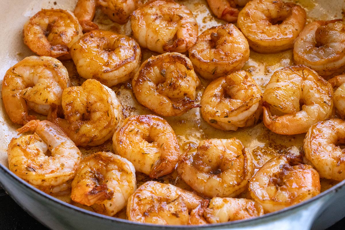 Several pieces of shrimp searing in a large pan.