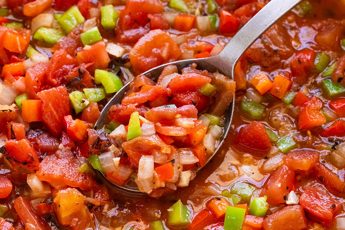 Fire roasted tomatoes and bell peppers sauteed in a pan.