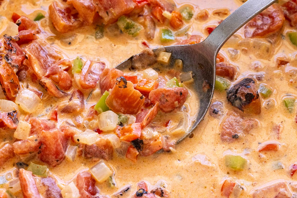 Cream sauce being mixed with sauteed vegetables.